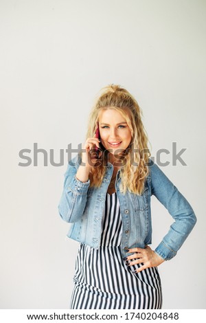 Always in touch. Beautiful girl in striped summer dress is talking on phone and smiling with a white background. Vertical picture