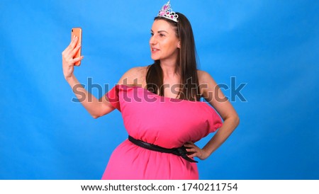 The most beautiful girl in a pink dress from pillows makes a selfie on a blue background. Crazy quarantine. Fashion 2020. Put on a pillow. Challenge 2020 due to house isolation.