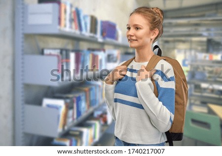 education, travel and tourism concept - happy smiling teenage student girl with school bag or backpack over book shelves in library on background