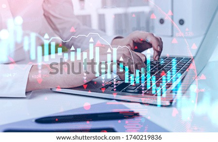 Hands of businesswoman typing on laptop at blurry office table with double exposure of falling financial chart. Concept of crisis and stock market. Toned image