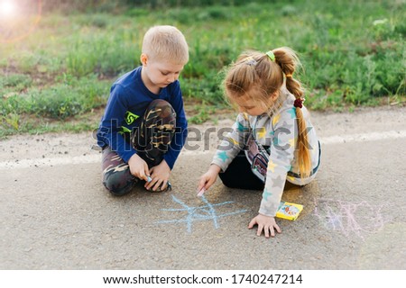 Beautiful boy and girl twins draw on the pavement with colored crayons. International Children's Day.