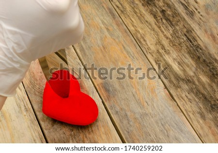 Woman's hand in white gloves with a knife pierces a red heart on a wooden background, copy space.