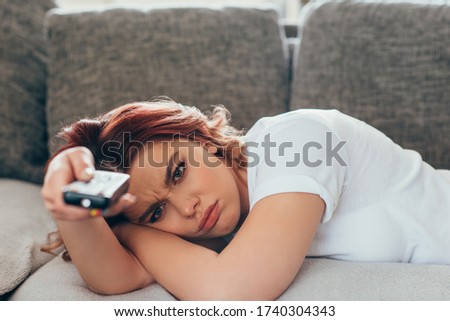 angry girl with remote controller watching tv at home on quarantine