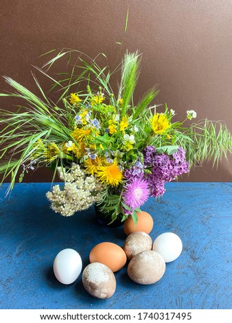 Multi-colored Easter eggs and bright wild flowers in a decorative vase, against a background of an abstract surface. Free space.