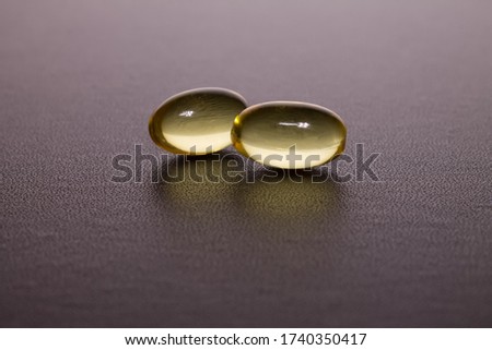two yellow transparent omega-3 capsules lie against a dark background