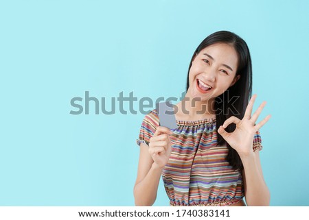 Beautiful young Asian girl holding blank credit card and ok hand women on background blue isolated. Asia women happy smile and copy space 