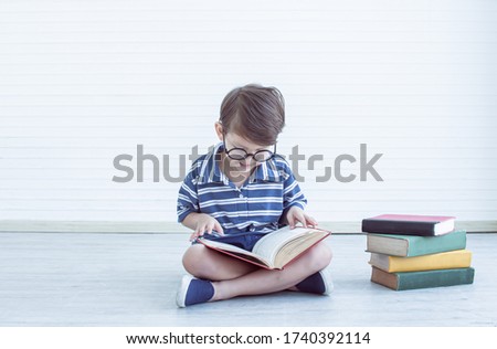 Little caucasian nerd boy wearing glasses and reading books at home with copy space on the left side. Education concept.