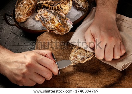 Shucking an oyster, man's hands with a special knife, opening oysters on a wooden board Royalty-Free Stock Photo #1740394769