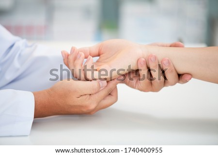 Asian doctor examining patient with wrist bone problems painful wrist caused by prolonged work on the laptop. Carpal tunnel syndrome, arthritis, neurological disease concept. Numbness of the hand