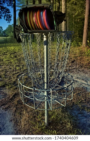 Disc golf basket with a bag of discs on top of it.