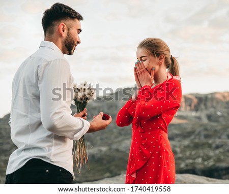 A man stands on his knee near the cliff and makes a creative proposal to a woman traveling in trolltunga, Norway. Emotional couple in love, engagement, rocks, nature, fjords. She said yes on the top. Royalty-Free Stock Photo #1740419558