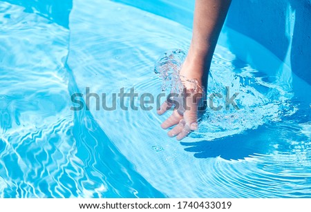 A young woman's hand touches the clear blue water in the pool. Beautiful summer day in the pool, place for text, horizontal bright photo
