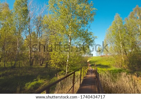 Pleasant sunny summer landscape: old blue sky and clouds, green grass and a river lake artificial channel and an old bridge. A happy idyllic scenery view.