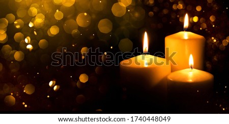 Burning candles with festive bokeh on a black background. Holiday concept.