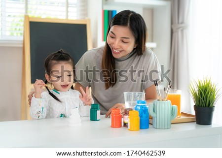 Asian kindergarten school girl with mother painting Plaster doll with Acrylic water color paint in living room at home. Homeschooling and distance learning.
