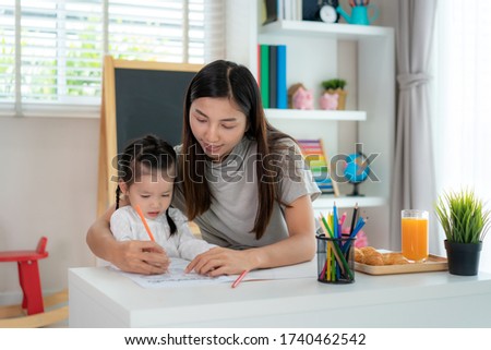 Asian kindergarten student girl with mother painting picture in book with color pencil at home, Homeschooling and distance learning.
