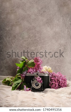 Old vintage camera framed by purple and white lilac flowers. Bouquet of lilacs and retro camera. Vertical photo with copy space in the upper part of photo.