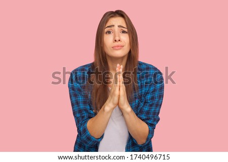 Please! Portrait of girl in checkered shirt holding hands in prayer, looking with imploring pleading expression, begging help, asking forgiveness. indoor studio shot isolated on pink background Royalty-Free Stock Photo #1740496715