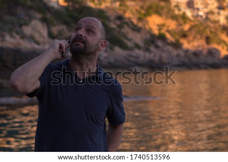 A man taking photos at sunset in Cala Llamp with his mobile phone. Beach cove in Mallorca