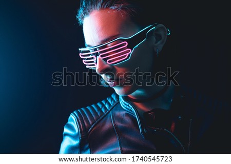 Young girl with colored neon glasses wearing black leather jacket and slicked back hair on black background. Blue and pink lights
