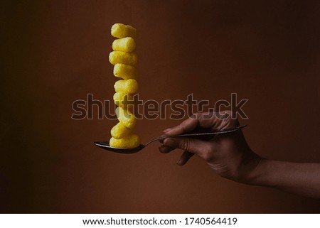 Yellow corn sticks are stacked on a metal spoon held by a hand. Brown background. Abstract picture. Unusual food photo.