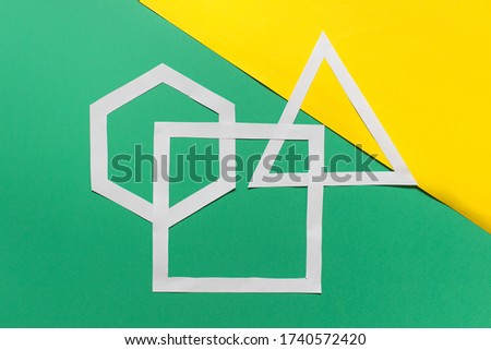 Three handmade paper geometric shapes hexagon, triangle, square arranged on green yellow background.