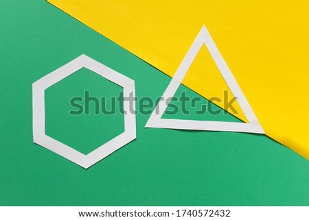 Two handmade paper geometric shapes hexagon and triangle arranged on green yellow background.