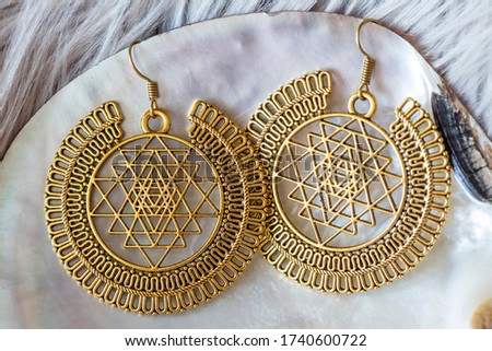 Metal earrings in sacred geometry sri vantra shape on white pearl shell background