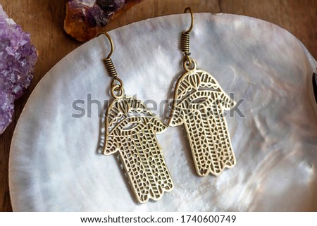 Metal earrings in hamsa fatima hand shape on white pearl shell background