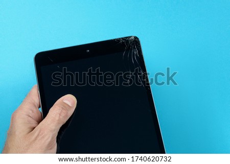 Male hand holding a cracked tablet on blue background
