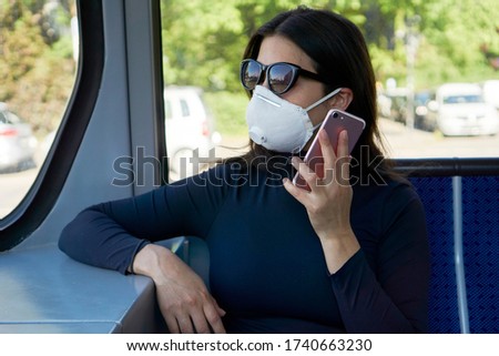 A pretty brunette woman with FPP2 mask and talking on the cell phone in the tram. Royalty-Free Stock Photo #1740663230