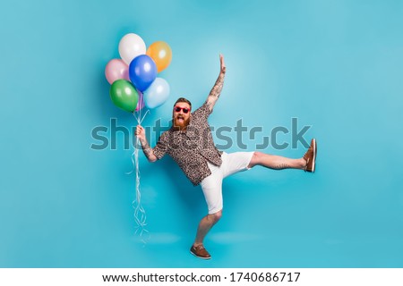 Full size photo of crazy luxury person guy hold many colorful air balloons festive event party raise hand leg wear leopard shirt sun specs shoes shorts isolated blue background