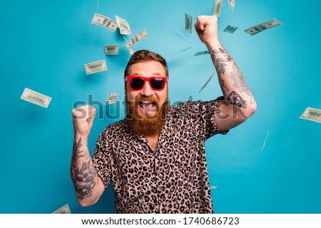 Photo of crazy handsome guy luxury rich person dollars fall from sky lottery cashback open mouth win big money raise fists wear leopard shirt sun specs isolated blue background