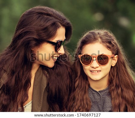 Happy fashion daughter smiling with her mother in trendy sunglasses on nature summer background. Closeup toned color portrait