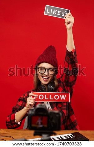 Excited blogger with placards looking at camera while sitting at the table against the red wall