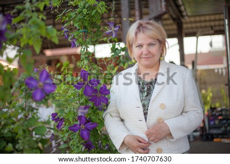 Happy senior woman with blond hair on the background of violet flowers. Nature backgrounds, 
