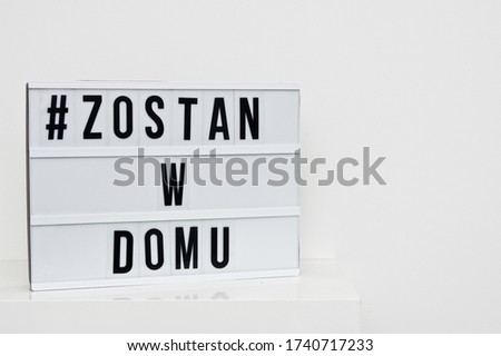 Stay at home message on white board in Polish language agains white wall with copy space.