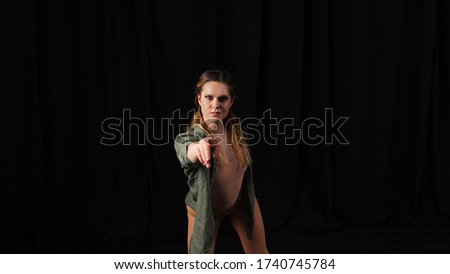 Young woman on an isolated black background shows with index finger at you, creative girl, facial expressions