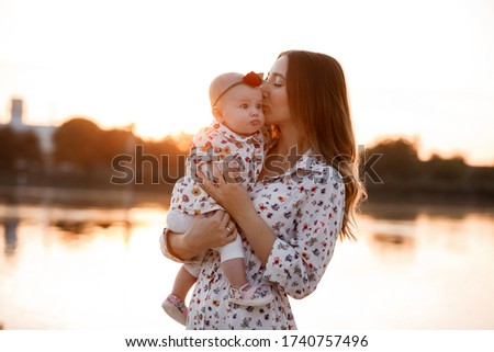Mum, little daughter outdoors. Young mother with baby girl walk on beach near lake on sunset. Family holiday on pond. Portrait mom with child together in nature. Happy Mothers Day.