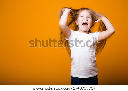 Beautiful little girl child raises her hands up and smiles on an orange background.