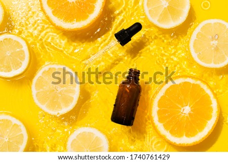 Cosmetic bottle product serum vitamin C with orange and lemon flat lay on yellow background clean water splashing, top view, copy space Royalty-Free Stock Photo #1740761429