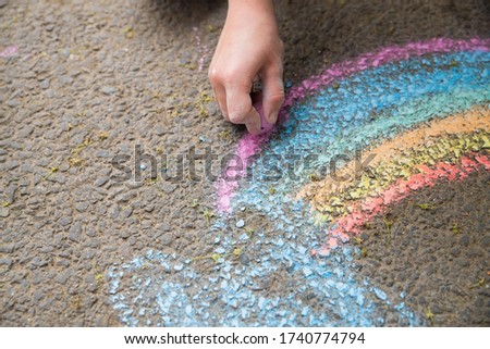Children's hand draws a rainbow on the asphalt. Close up. Childhood. Crayons. Space for copying.
