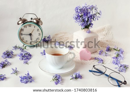 The concept of good morning and good mood : a Cup of tea, an alarm clock and a bouquet of blue flowers on the table with a pink heart, side view