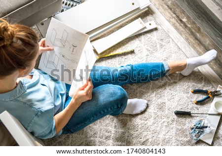 Concentrated young woman reading the instructions to assemble furniture at home in the living room Royalty-Free Stock Photo #1740804143