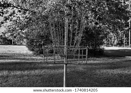 Black and white picture of a disc golf basket in a field.