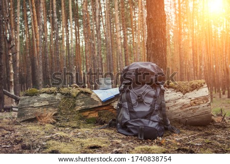 Tourist backpack, metal mug and map in the forest. Concept of a hiking trip to the forest or mountains