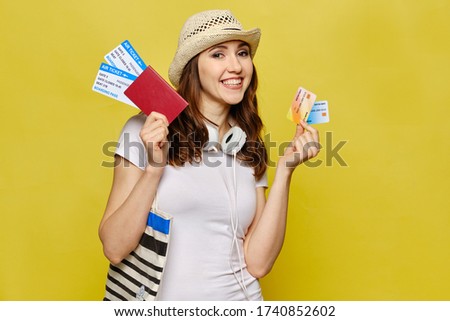A beautiful girl in casual clothes is holding a passport and airline tickets with credit bank cards. Portrait of a caucasian woman.