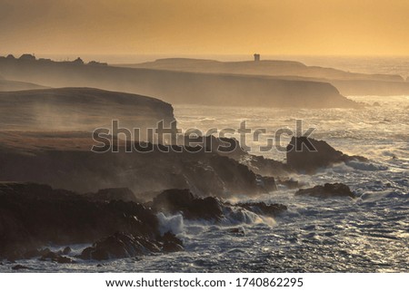 An aerial beautiful shot of a wavy sea against the cliffs under an orange sky at sunset