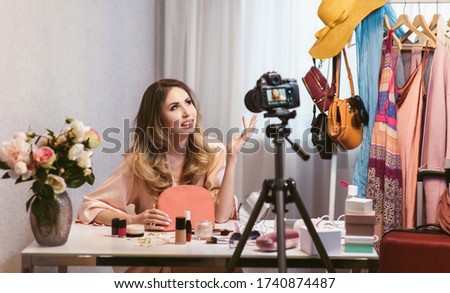 Girl recording a fashion blog. A young woman blogger talking about a handbag from a new collection on camera while she making a new vlog issue. DSLR camera on tripod in the foreground