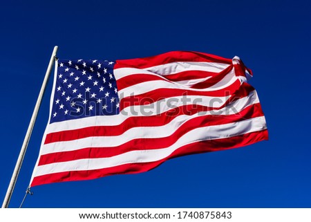 American flag is flowing in the wind on blue sky background.
